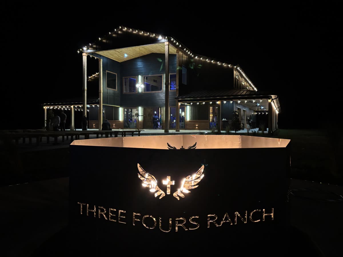 The illuminated Three Fours Ranch monument sign at night, with the lit venue behind it