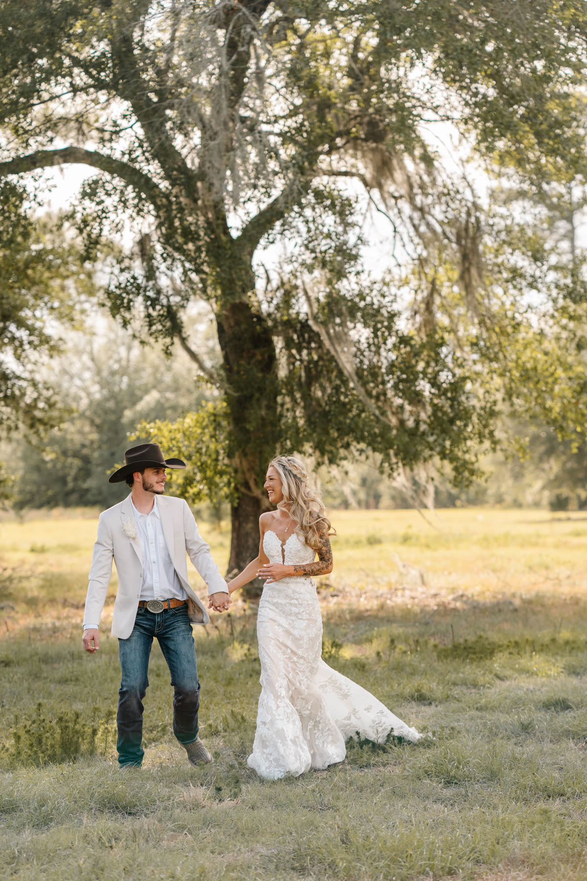 A bride and groom walking hand in hand through the golden pasture at sunset