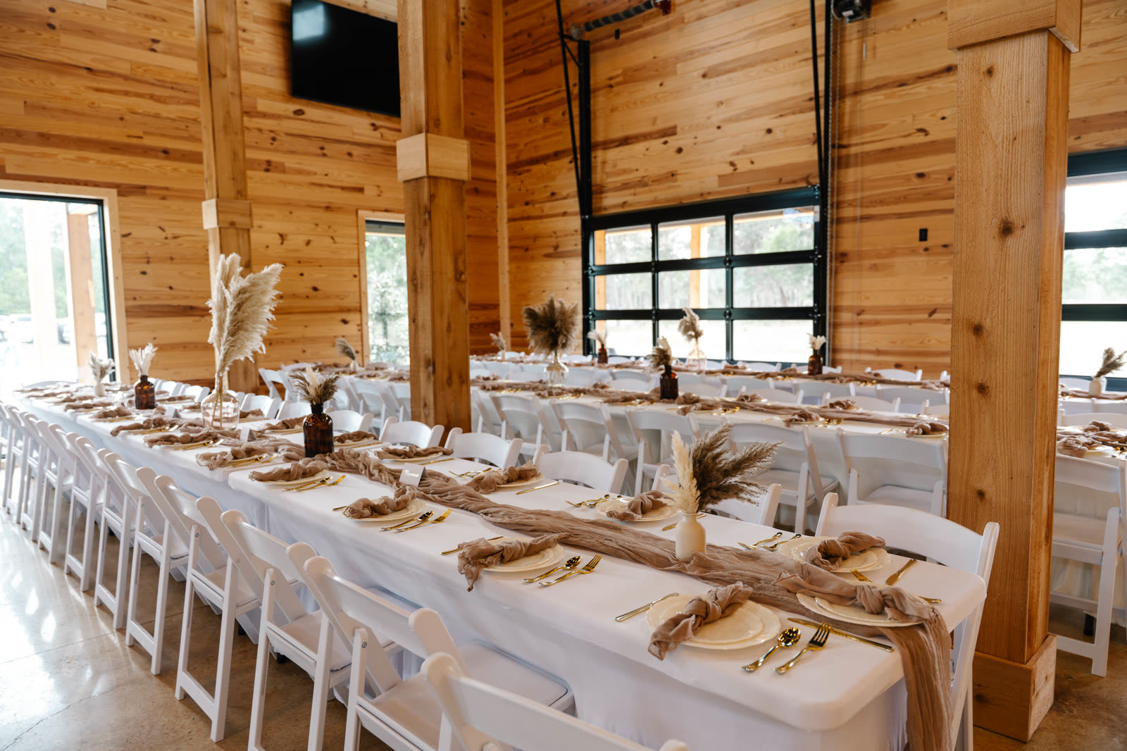 Long banquet tables dressed in white linen and blush gauze runners inside The Venue's pine-clad hall