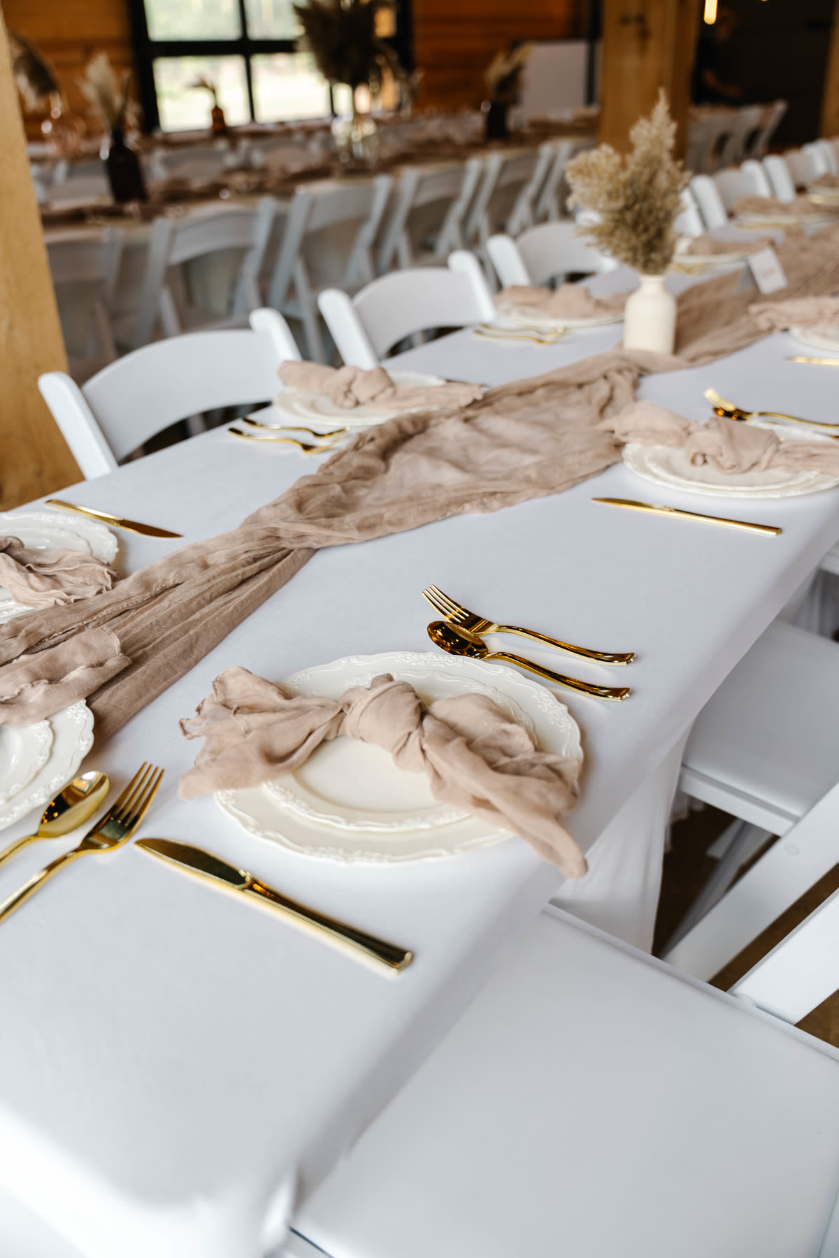 Place setting detail with gold flatware, scalloped china and a knotted blush gauze napkin