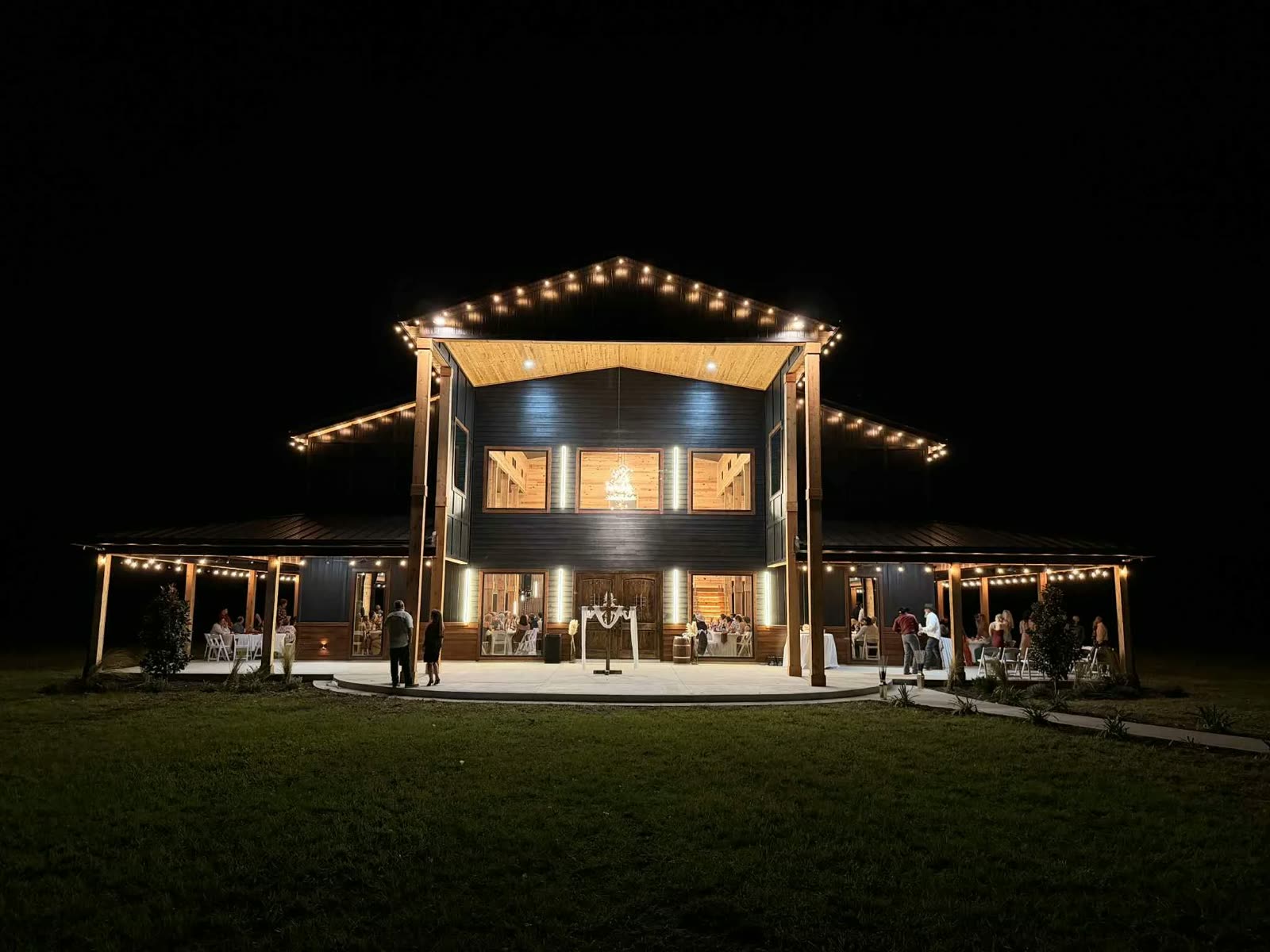 The Venue after dark, every gable and wraparound porch strung with lights, guests spilling onto the lawn