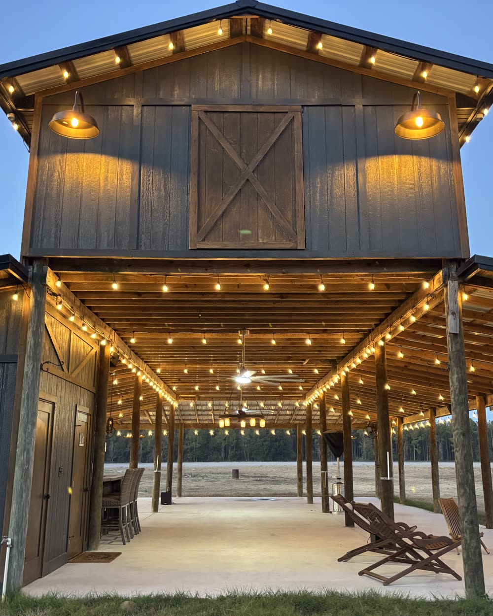The open-air Pole Barn lit with string lights at dusk